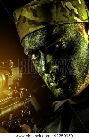 A soldier in war paint looks through the scope of automatic rifles. Military, war. Special forces.