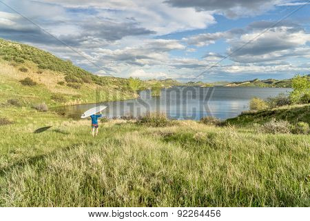 male paddler is carrying hi SUP paddleboard to a lake - Horsetooth Reservoir near Fort Collins, Colorado, at springtime