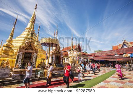 Buddhist people praying and walking around a golden pagoda.