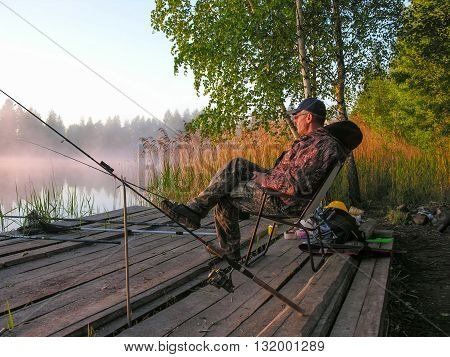 Fisherman meets sunrise on the bank of forest lake