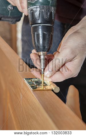 Door installation Close-up of cordless drill screwdriver in his hand carpenter tightening screws for fastening brass hinges to a wooden interior door.