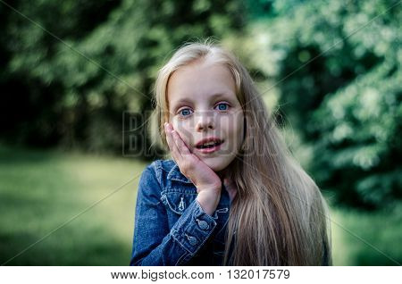 Surprised cute little blond girl at summer field.