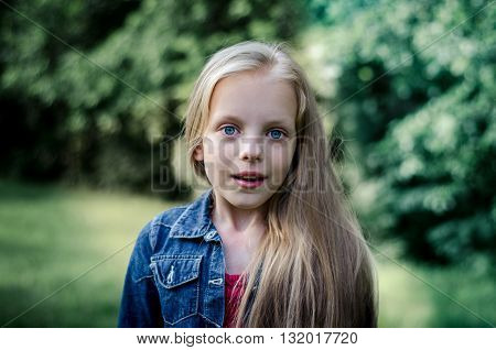 Surprised cute little blond girl at summer field.