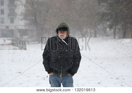 Older man with greybeard in senior fifty on snowstorm outside in the park