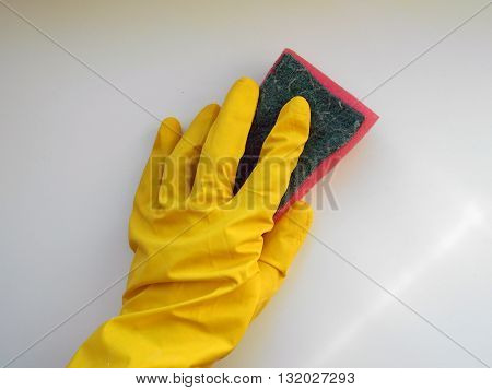Hand in rubber glove holds a sponge to wash the surface. The glove protects hands skin against chemical effects of detergents.
