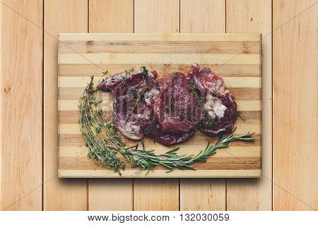 Fresh beef steak ready for BBQ cooking. Raw meat on a cutting board with rosemary leaf top view at wood. Raw beef, veal meat on wood, closeup. Marinated in spices raw steak for barbecue.