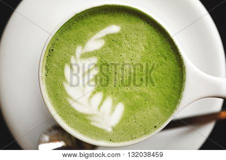 Cup of green tea matcha latte with latte art, standing on wooden table.