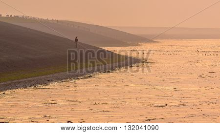Person Walking On Sea Dike In Orange Haze