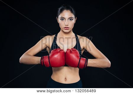 Young fitness girl with bloxing gloves looking at camera over black background