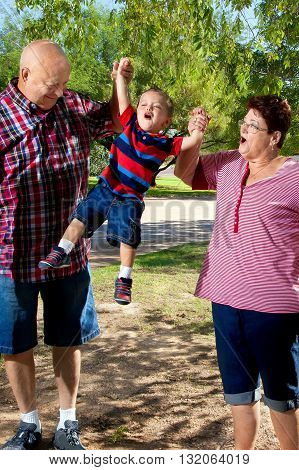 A grandpa and grandma lift their grandson into the air. Grandma is looking at her grandchild with a face as if she is making sound effects.