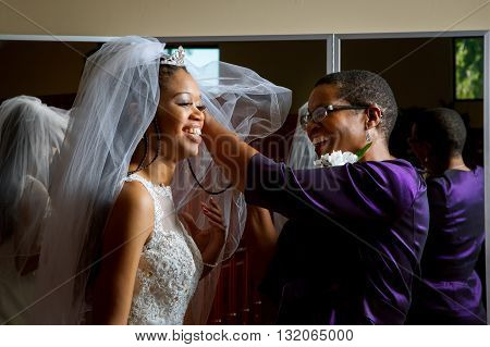 Mother of the bride adjusts her daughter's veil on her wedding day. Beautiful African American women smiling while getting the daughter ready for her wedding.