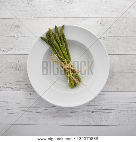 Overhead view of freash green asparagus on a white plate over a retro wooden background