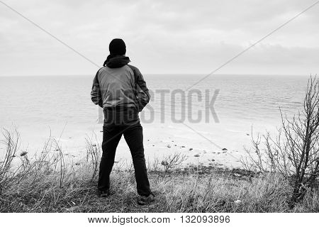 Man In Windcheater Stand On Cliff Above Bay And Looki At Sea Far Horizon. Windy Cold Weather
