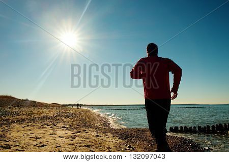 Tall Man In Dark Sportswer Running And Exercising On Stony Beach At Breakwater.