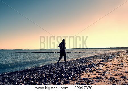 Tall Man In Dark Sportswer Running And Exercising On Stony Beach At Breakwater.