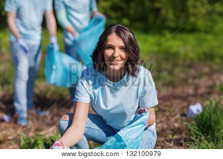 volunteering, charity, cleaning, people and ecology concept - happy woman and group of volunteers with garbage bags cleaning area in park