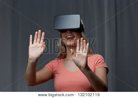 technology, virtual reality, entertainment and people concept - happy young woman with virtual reality headset or 3d glasses playing game at home and touching something invisible