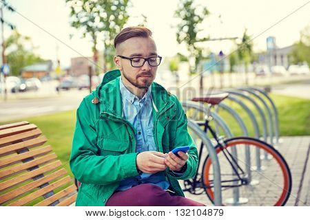 people, style, technology and lifestyle - happy young hipster man with smartphone and fixie bike sitting on bench in city