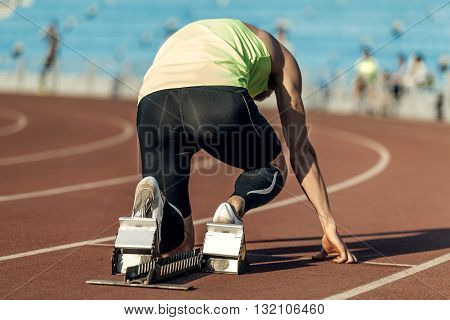 male athlete in starting blocks. running at sprint at stadium