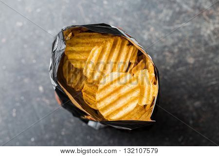 Crinkle cut potato chips on kitchen table. Tasty spicy potato chips in bag. Top view.