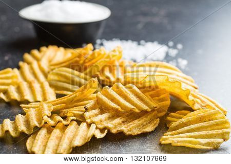 Crinkle cut potato chips on kitchen table. Tasty spicy potato chips with salt.