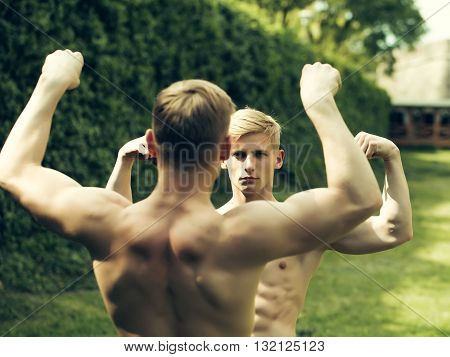 Muscular young twins bodybuilders with beautiful sexy body and bare torso posing outdoor sunny day on natural background