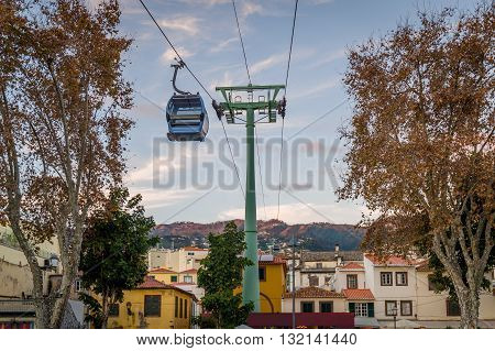Cable car is going over the old town of Funchal. Touristic district of the city, sunset warm light and mountain range on the background. Funchal, Madeira island, Portugal.