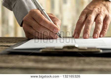 Front view of male hands signing document contract or application form on a clipboard with ink pen low angle view.