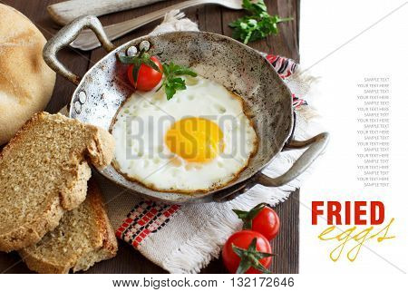 Fried egg with tomatoes homemade bread and herbs on a old frying pan on wood