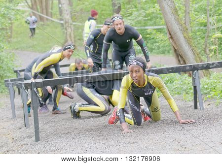 STOCKHOLM SWEDEN - MAY 14 2016: African woman and competitors crawling under bars in the obstacle race Tough Viking Event in Sweden May 14 2016