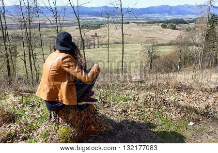 Lonely girl in forest sitting on tree