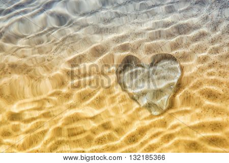 Rippled under water Heart distortion, blurred wave action over glass heart on beach