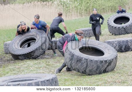 STOCKHOLM SWEDEN - MAY 14 2016: Group of men and woman struggling to tip a large tractor tire obstacle in the obstacle race Tough Viking Event in Sweden April 14 2016