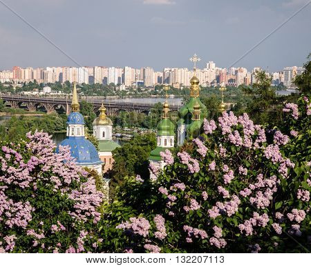 Orthodox cross on a background of the sky and the city in purple flowered garden