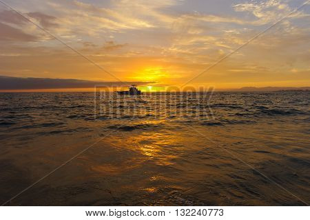 Boat sunset is a sport fishing boat at sunset trolling with fishing poles waiting for a strike.
