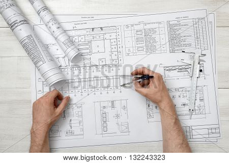 Close-up hands of man holding an engineering divider over drawing plan in top view.  Workplace of architect or constructor. Engineering work. Construction and architecture. Architect drawing. Measurement. Draftsmanship.