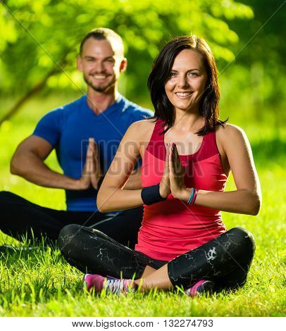 Young man and woman doing yoga in the sunny summer park. Couples Yoga on green grass outdoor.