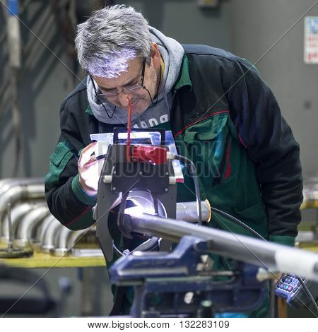 Industrial operator setting  computer controlled process of orbital welding machine in  stainless steel pipes manufacturing workshop.