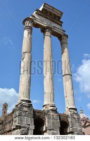 Ruins of the ancient Temple of Castor and Pollux (Dioskouri) in Roman Forum in the center of Rome with Capitol Tower and baroque dome