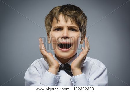 Closeup Portrait of handsome boy with astonished expression while standing against grey background.