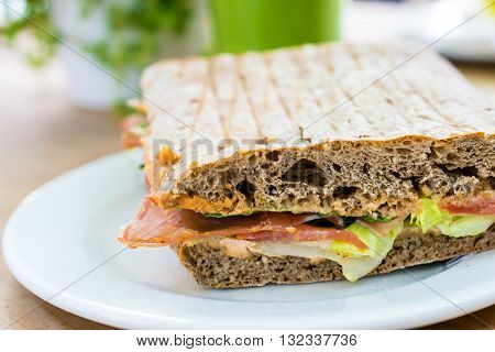 Sandwich with ham, tomato, rucola und salad serviert with smoothie on wooden table.