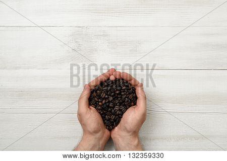 Close-up hands of man holding a handful of coffee beans. Top view composition. Workplace coffee maker. Top view. Coffee house. Uplifting mood. Coffee break.