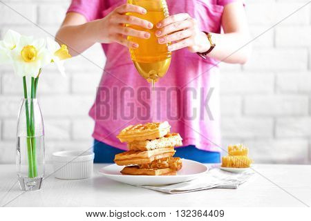 Woman pouring honey on waffles