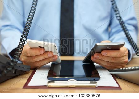 busy businessman in office at the desk using two mobile phones two telephones and tablet computer