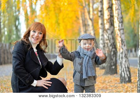 Heppy mother stends with a cheerful toddler in the park in autumn.