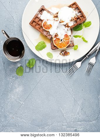 Belgian soft waffles with blood orange, cream, marple syrup and mint on white plates over concrete textured background. Top view, copy space