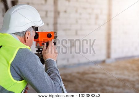 Orange tool.  Busy and serious man working hard with a help of a level standing in a new building