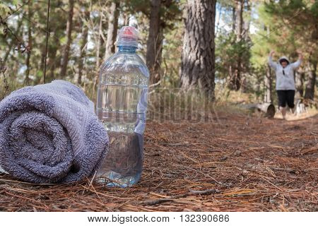 Overweight woman jogging on forest trail with waterbottle and towel in the foreground
