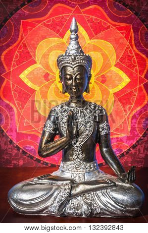 Silver Buddha staue with warm colored mandala background