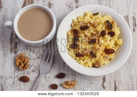 Cooked millet groats with raisins and walnuts on white plate cup of coffee with milk concept of healthy food nutrition and nutritious breakfast